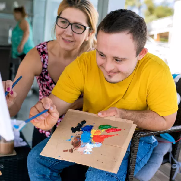 Disabled man painting with carer