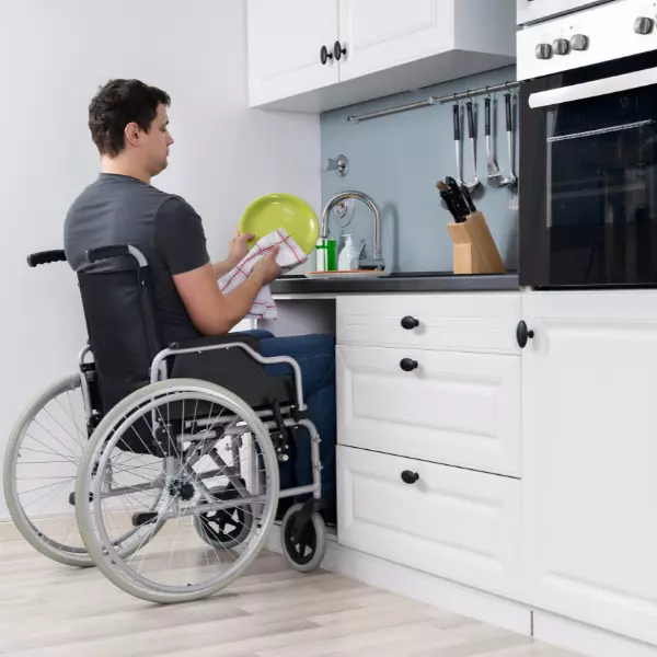 Disabled man in wheelchair doing dishes at modified sink in home
