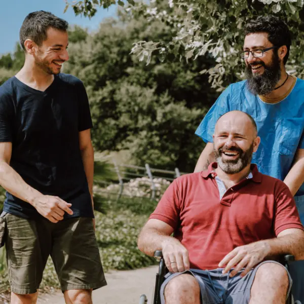 Disabled man in wheelchair smiling outdoors with 2 friends